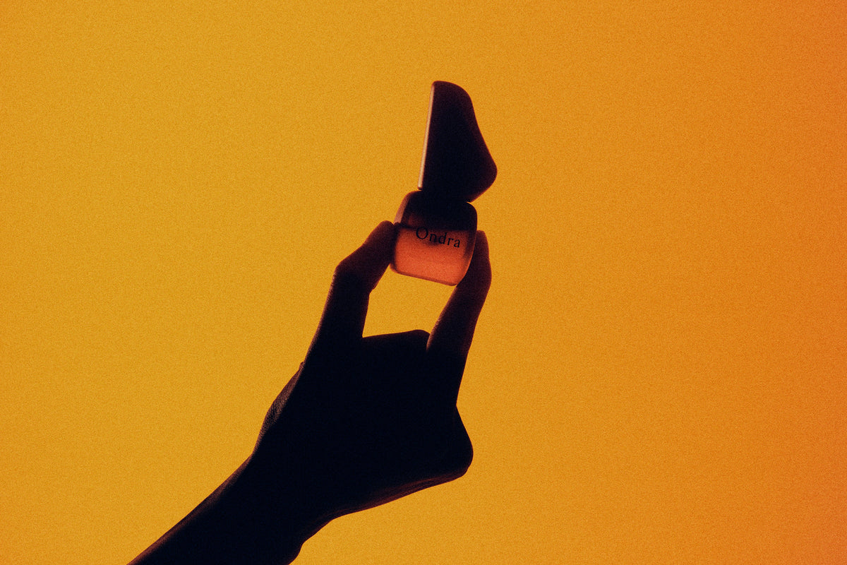 A hand holding an ONDRA bottle against an amber background