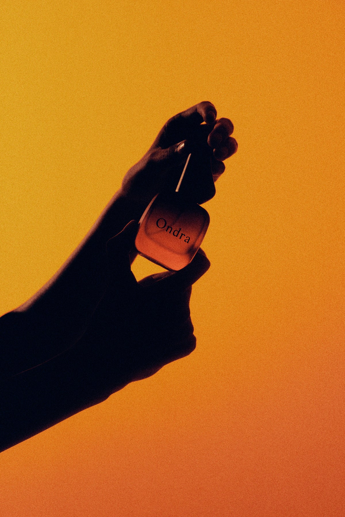 Hand holding an ONDRA bottle against an amber background